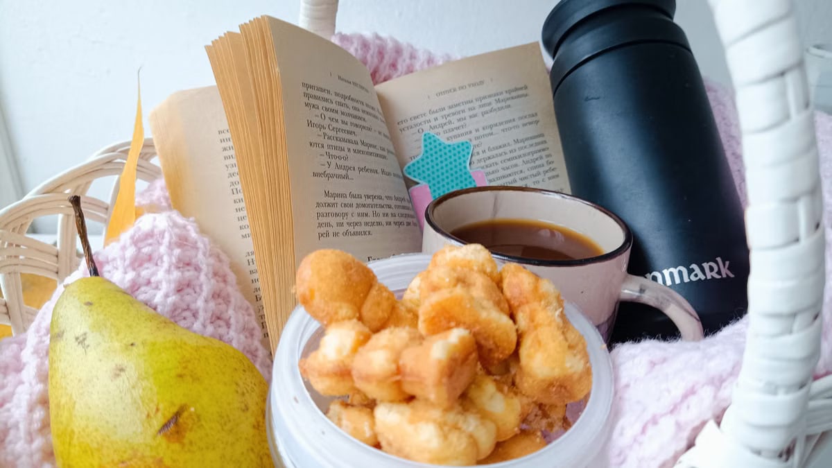 A cozy setup featuring a book, snacks, coffee, and a pear in a basket.
