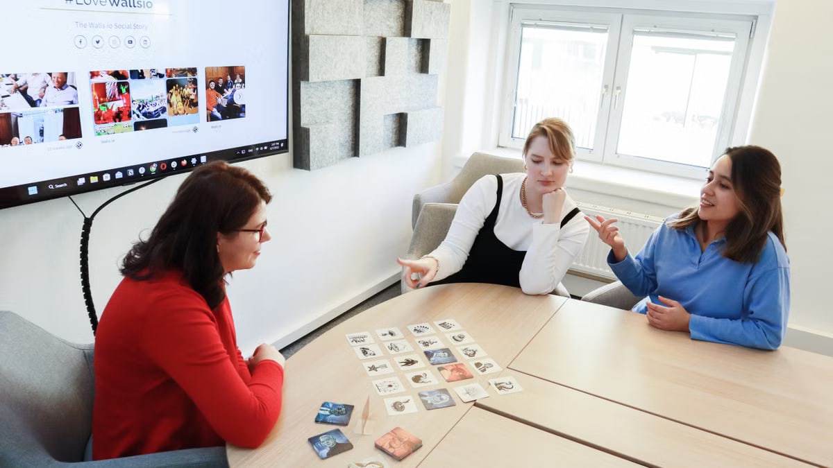 Three women engaging with cards around a table in an office environment, discussing ideas.